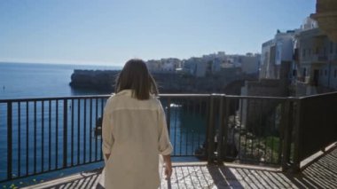 Genç bir İspanyol kadın polignano 'da güzel bir manzaranın tadını çıkarıyor. Bir kısrak, puglia, İtalya, manzaralı bir sahil kasabası ve arka planda sakin mavi bir deniz..