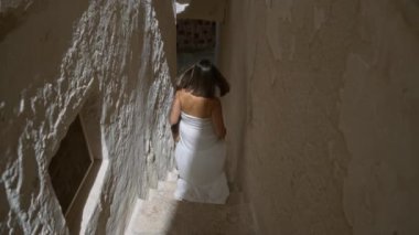 Beyaz elbiseli genç bir İspanyol kadın, eski bir kasaba olan Ostuni 'de dar bir taş merdivenden aşağı yürür. Puglia, İtalya, güneş ışığı altında yıkanır..