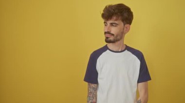 Yüzünde doğal mutlu bir ifadeyle genç, neşeli İspanyol bir adam, kenara çekilip, izole edilmiş sarı bir arka planı işaret ediyor ve gülümsüyor..