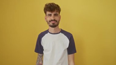 Neşeli, İspanyol asıllı genç bir adam. Başarı işareti gösteriyor. Sarı arka planda izole bir şekilde kameraya doğru bakıyor.