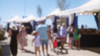 Güneşli bir Mallorca gününde açık hava pazarında mavi çadırlarla yürüyen bulanık insanlar.