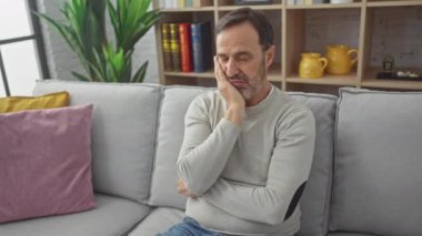 Bunalımlı orta yaşlı bir adam, sıkılmış ve yorgun, evde sorunlar üzerine kafa yoruyor, kollarını kavuşturuyor, süveterinin altında düşüncelere dalmış.