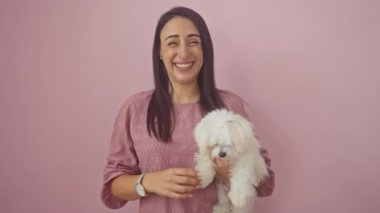 Genç, mutlu İspanyol bir kadın köpek ayakta duruyor ve kenarı işaret ediyor, gülümseyen bir el evcil hayvanının üzerinde, izole edilmiş pembe bir arka planda dinleniyor.