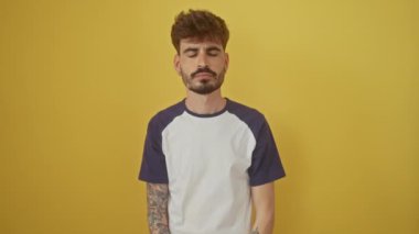 Sinirli genç İspanyol adam parmaklarıyla kulaklarını kapatıyor, izole edilmiş sarı arka planda duruyor, gürültüye dayanamıyor, sağırlık ve acıyı ifade ediyor.