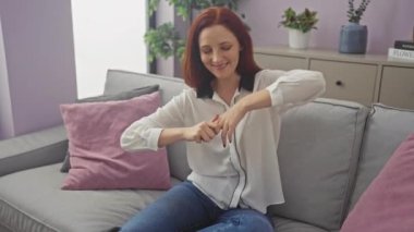 Kızıl saçlı kadın evdeki kanepede dinleniyor, modern iç mekanda rahat ve mutlu görünüyor..