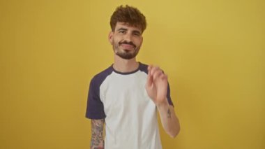 Genç, mutlu, İspanyol asıllı bir adam ayakta duruyor, dört numarayı işaret ediyor ve parmaklarıyla gösterirken izole edilmiş sarı bir arka planda gülümsüyor.