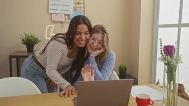 İki kadın rahat bir oturma odasında dizüstü bilgisayarla arkadaşlık ve teknoloji sergileyerek ev ortamında kaynaşıyor..