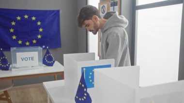 Avrupa Birliği bayraklı bir Avrupa seçim odasında genç sakallı adam oy kullanıyor