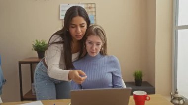 Konforlu, modern bir oturma odasında, takım çalışması ve teknoloji sergileyen bir dizüstü bilgisayarda işbirliği yapan iki kadın..