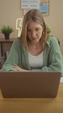 Samimi, modern bir ofis ortamında dizüstü bilgisayarla çalışan odaklanmış sarışın bir kadın..