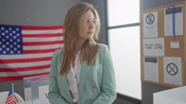 Spor ceketli kendine güvenen bir kadın Amerikan bayrağıyla bir Amerikan üniversitesi odasında duruyor.