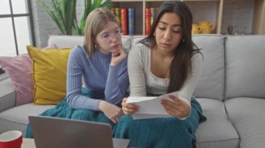 İki kadın, rahat bir oturma odasındaki dizüstü bilgisayarın yanındaki kanepede evrak işlerini tartışıyor..
