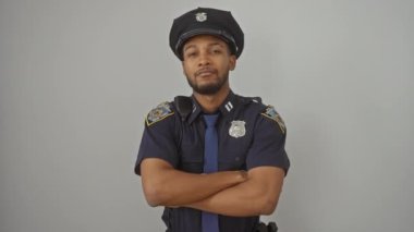 Sırıtan Afro-Amerikan bir adam. Polis üniforması giyiyor. Kollarını kavuşturmuş, ön tarafa bakıyor. Bu yakışıklı çocuktan yayılan doğal pozitiflik saf beyaz izole arka planda..