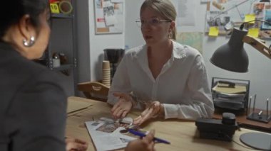 İki kadın, karmaşık bir dedektifin ofisinde dokümanlar ve fotoğraflar hakkında gergin bir tartışmaya girişirler..