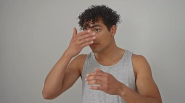 Askılı tişörtlü genç İspanyol bir adam. Kıvırcık saçlarını bembeyaz bir arka planda tarıyor..