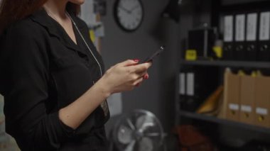 Dedektiflik bürosundaki genç bir kadın akıllı telefondan mesaj atıyor. Etrafı dosyalar ve duvar saatleriyle çevrili..
