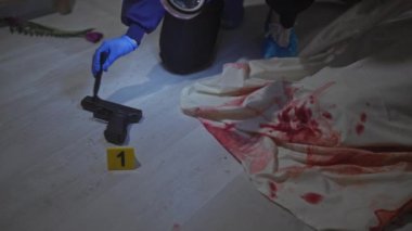 Dedektif kadın, kanlı bir suç mahallinde elinde büyüteç ve kanıt kalemiyle tabancayı inceliyor..