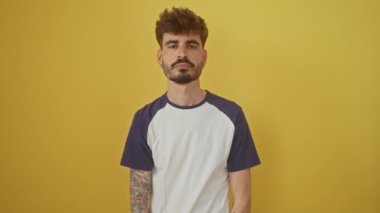 Sessiz İspanyol genç adam, parmakları dudaklarının üzerinde canlı sarı arka planda sessizlik istiyor, gizli bir duyguyu paylaşıyor.