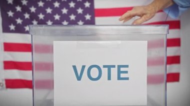 Amerika seçimlerinde oy veren kıdemli bir kadın, Amerikan bayraklarıyla birlikte bir sandık merkezinde..