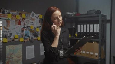 Ofiste odaklanmış bir kadın dedektif rozeti, telefonu ve soruşturma kuruluyla kanıtları analiz ediyor..