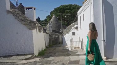 Yeşil elbiseli genç bir İspanyol kadın İtalya 'nın alberobello kasabasında yürüyor. İkonik Trulli evleri ve dar, beyaz yıkanmış caddeleriyle karakterize ediliyor..