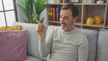 Neşeli orta yaşlı bir adam, neşeyle sırıtıyor ve sıcak evinin bir tarafını işaret ediyor, samimi yüzünü aydınlatan sıcak bir gülümseme.