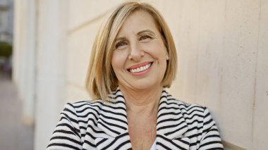 Gülümseyen beyaz, orta yaşlı bir kadın şehir sokaklarında.