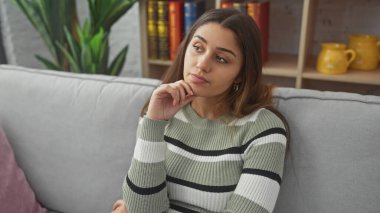 Düşünceli, genç bir İspanyol kadın rahat bir evin içinde, kanepede uzanıyor, zarafet havası yayıyor..