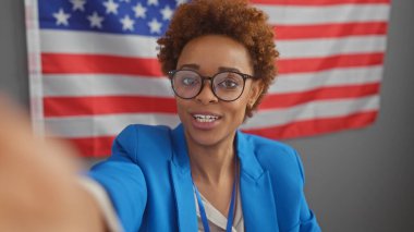 Afrika kökenli Amerikalı bir kadın, kapalı bir ortamda Amerikan bayrağıyla selfie çekiyor..