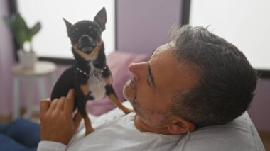 Orta yaşlı İspanyol bir adam evde küçük bir chihuahua köpeğiyle oturma odasında dinleniyor..