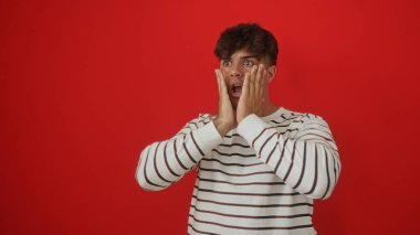 Şok olmuş, elleri yüzü üstünde, kırmızı arka planda kalmış genç bir İspanyol..
