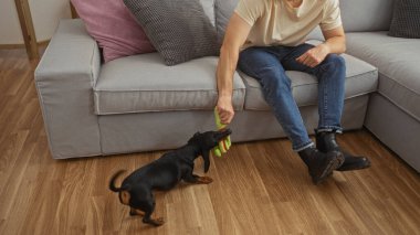 Samimi bir oturma odasında oyuncak taşıyan bir köpekle oynayan adam, evcil hayvan ve ev sahibi arasında bir bağ olduğunu gösteriyor..