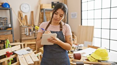 Genç bir İspanyol kadın, ahşap ve aletlerle çevrili iyi donanımlı bir marangoz stüdyosunda notlar alıyor..
