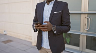 Yakışıklı Afro-Amerikan takım elbiseli adam şehir caddesinde akıllı telefon kullanıyor..