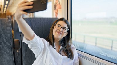 Genç ve güzel İspanyol kadın gülümsüyor. Tren vagonunda oturan akıllı telefonuyla selfie çekiyor.