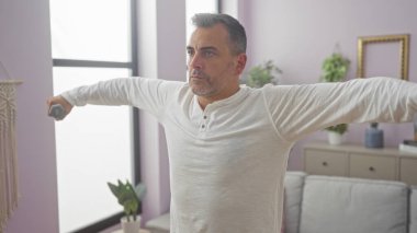 Yakışıklı, gri saçlı İspanyol bir adam evinin oturma odasında beyaz bir gömlek giyerek egzersiz yapıyor..