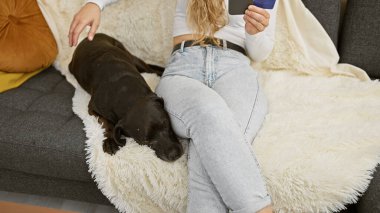 Kredi kartı olan genç bir kadın rahat bir oturma odasında uyuyan bir labrador 'un yanında oturuyor..