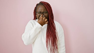 African american woman with braids dressed in white on a pink background pinching her nose clipart