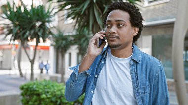 Şehirli bir sokakta telefonda konuşan kıvırcık saçlı, yakışıklı, genç bir adam..