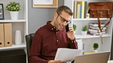 Ofiste gülümseyen İspanyol bir adam. Belgeleri incelerken telefonla iş yapıyor..