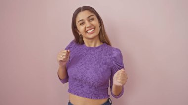 Mor bluzlu gülümseyen genç bir İspanyol kadın pembe izole edilmiş bir arka plana karşı güvenle poz veriyor..