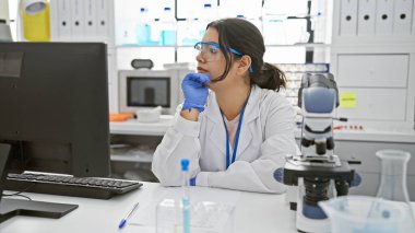 Teçhizat ve teknolojiyle çevrili bir laboratuvar ortamında düşünceli bir İspanyol kadın bilim adamı..