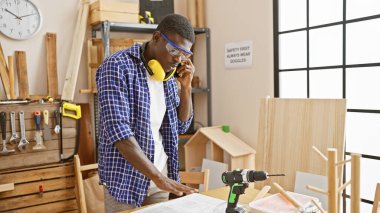 Marangozluk atölyesinde güvenlik ekipmanlı Afrikalı Amerikalı adam telefonda.