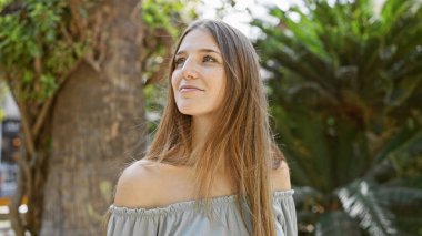 Genç, çekici sarışın bir kadın güneşin altındaki yemyeşil bir parka bakıyor..