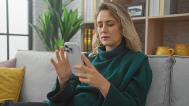 Beyaz kadın akıllı telefonu kapalı bir yerde kullanıyor, kanepede oturuyor, rahat bir oturma odasında..