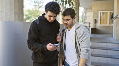 Şehir caddesinde akıllı telefon kullanan iki İspanyol adam..