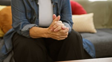 Oturma odasında elleri bağlı oturan düşünceli bir son sınıf öğrencisi, sükuneti ve olgunluğu yansıtıyor..