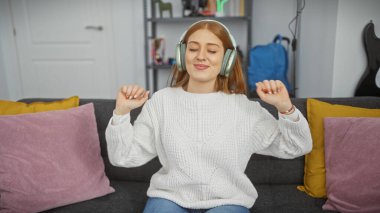 Genç beyaz kadın evde dans ederken kulaklıkla müzik dinliyor.