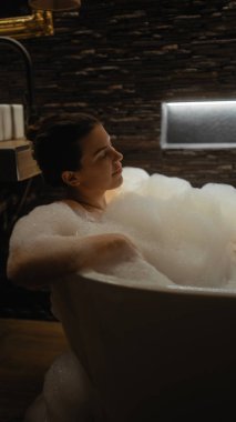 Huzurlu bir banyoda köpük banyosunun keyfini çıkaran rahat bir kadın.