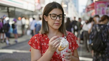Gözlüklü göz kamaştırıcı İspanyol kadın, Tokyo 'nun hareketli caddesinde yaz tatili sırasında lezzetli dondurmanın tadını çıkarıyor.
